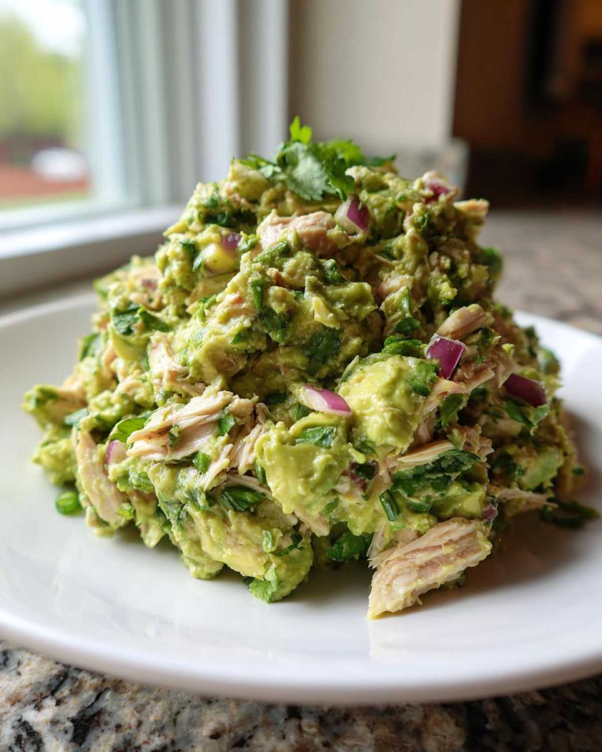 A generous serving of creamy avocado chicken salad mixed with red onion and cilantro, piled high on a white plate.