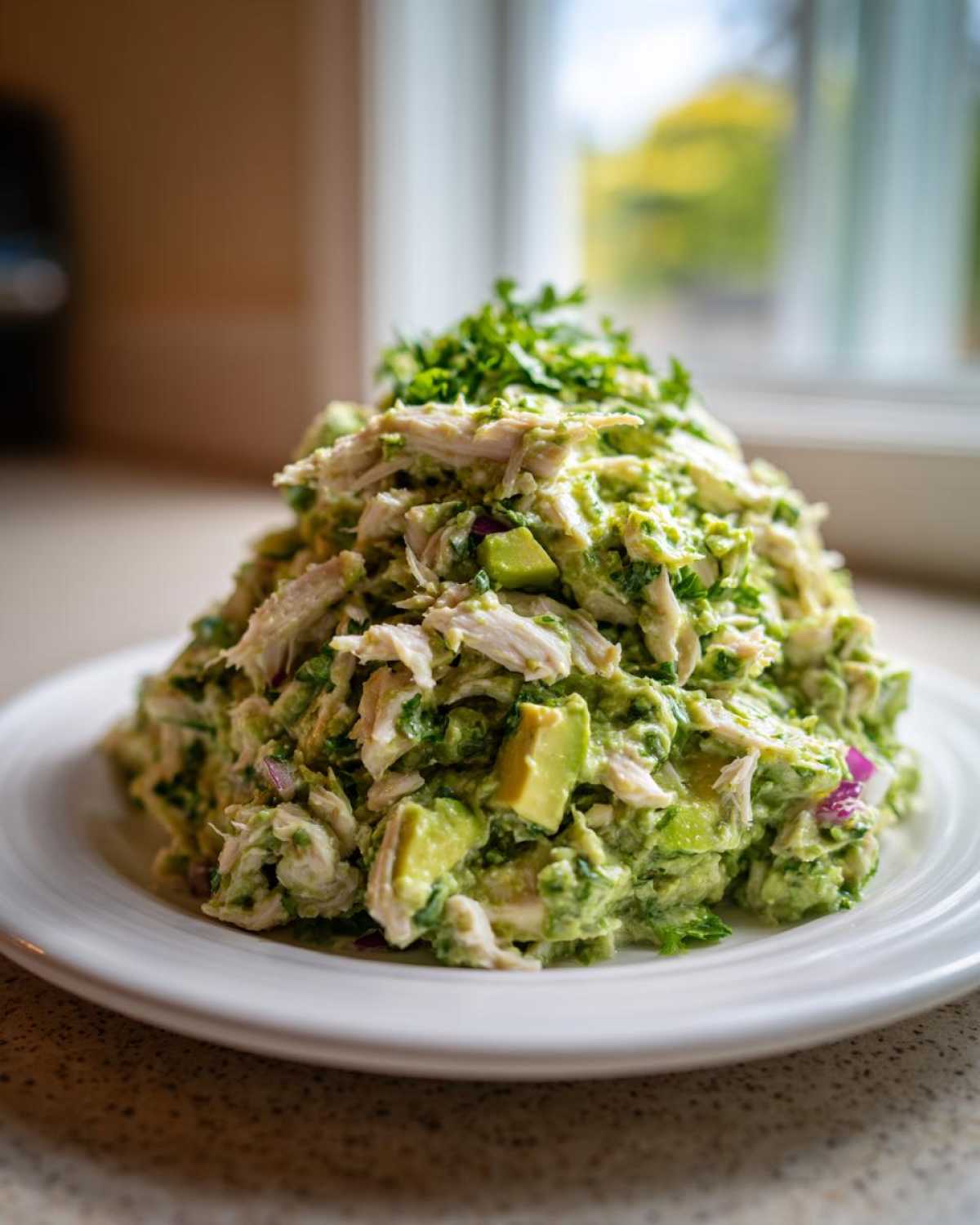 A generous mound of creamy avocado chicken salad with chunks of avocado and red onion, topped with fresh herbs.