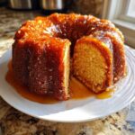 A golden Bacardi rum cake, bundt style, with a thick, glistening rum glaze pooling on the white plate.