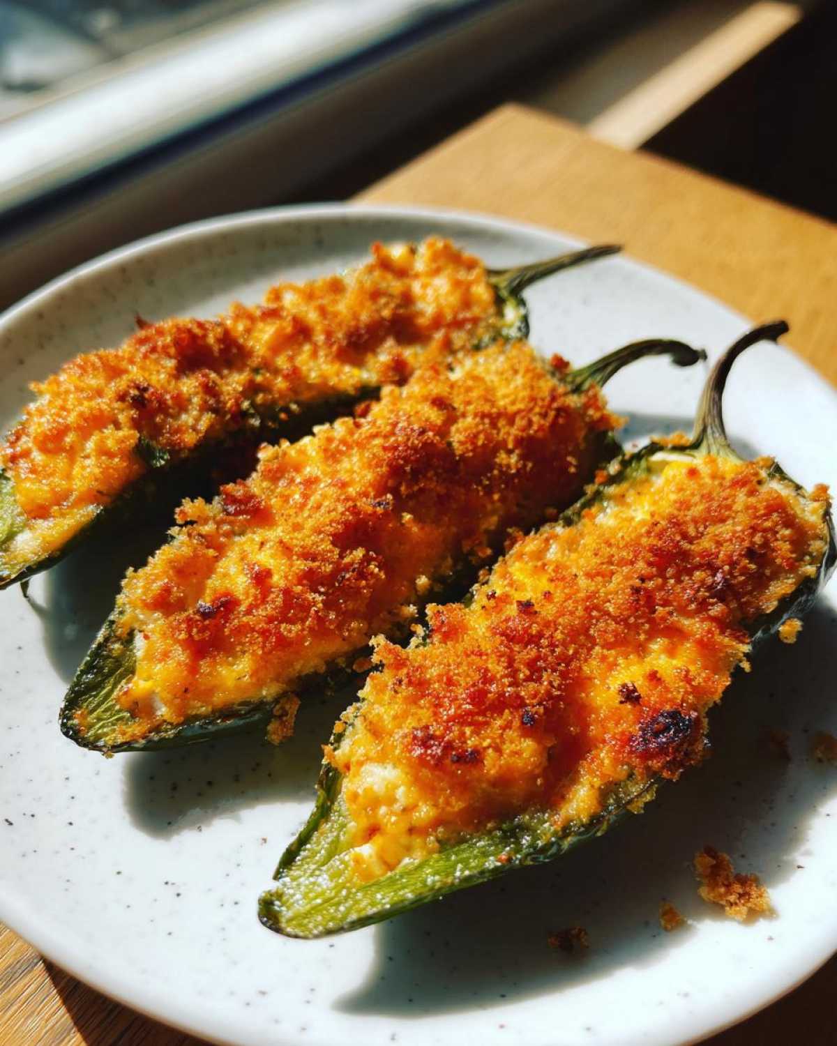 Three baked Jalapeño poppers stuffed with cheesy filling and topped with golden, crispy breadcrumbs.
