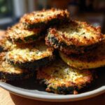 A stack of golden brown baked parmesan zucchini slices with crispy edges piled on a dark gray plate.