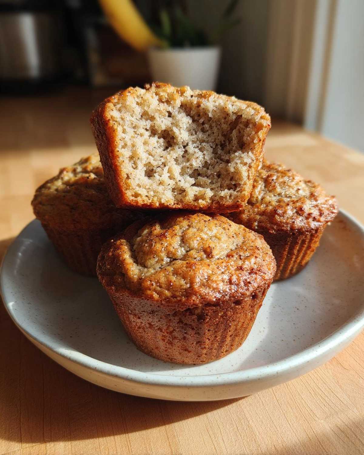 A stack of golden brown banana protein muffins, one cut in half showing the moist, textured interior.