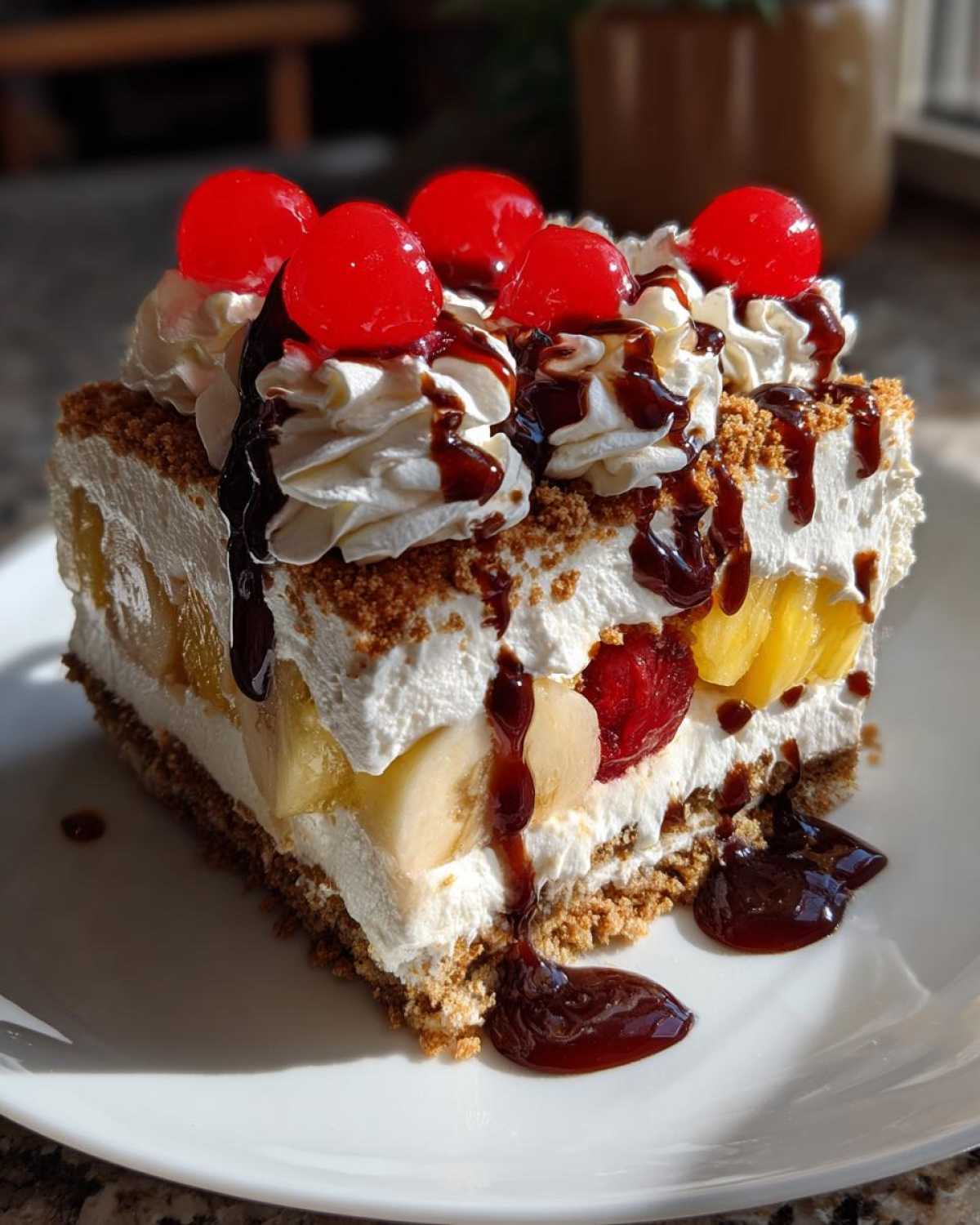A decadent slice of banana split cake topped with whipped cream, chocolate syrup, and maraschino cherries.