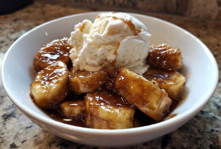 A white bowl filled with caramelized bananas foster and a scoop of vanilla ice cream melting on top.
