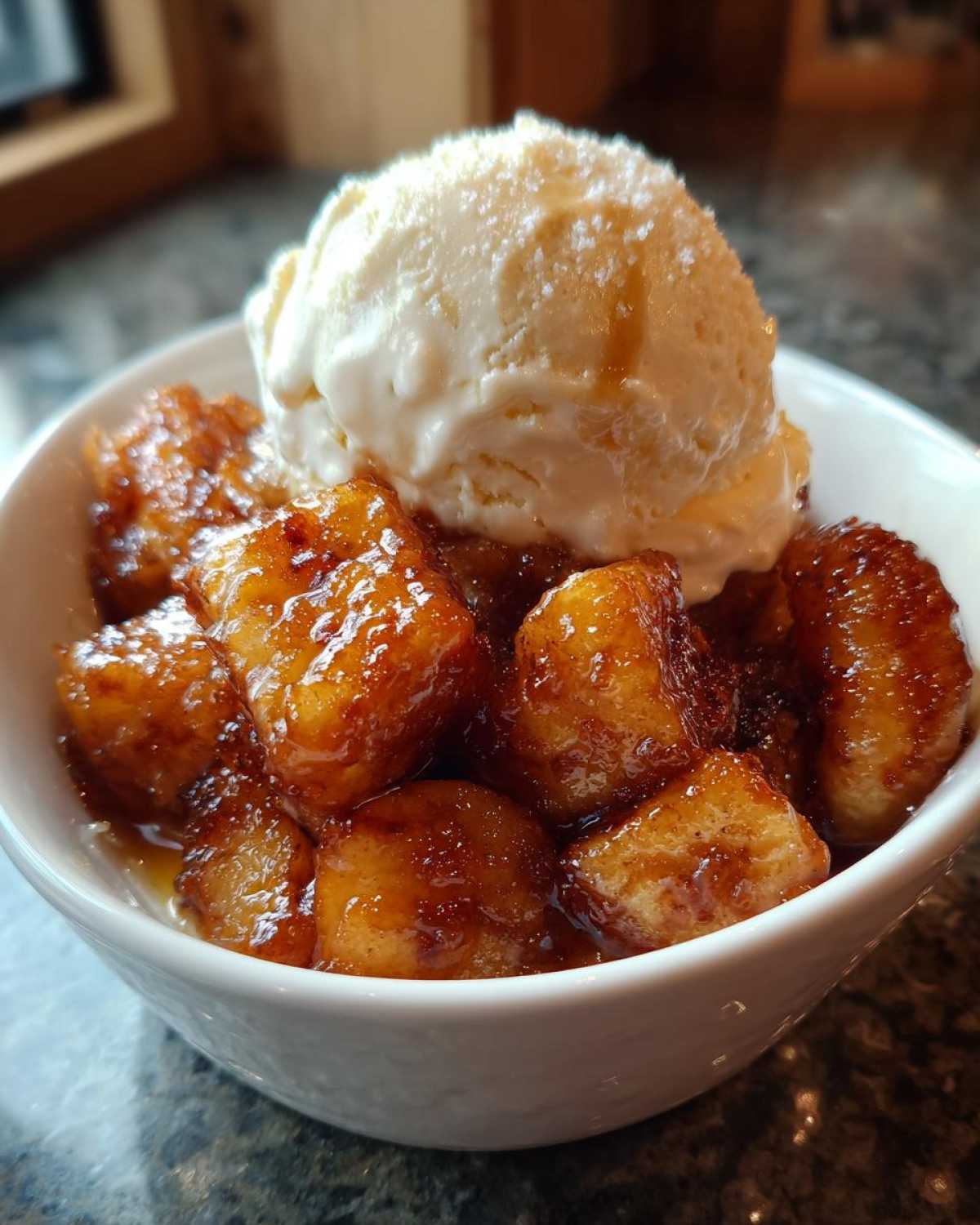 A close-up of rich, caramelized bananas foster topped with a scoop of vanilla ice cream in a white bowl.