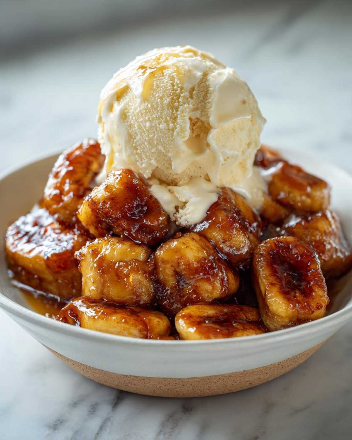 Close-up of rich, caramelized bananas foster topped with a melting scoop of vanilla ice cream.