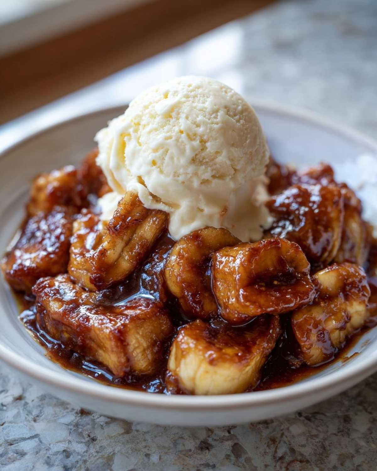Close-up of rich, caramelized bananas foster topped with a large scoop of vanilla ice cream.