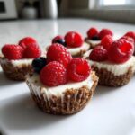 Close-up of several low-calorie cheesecake bites topped with fresh raspberries and blueberries.