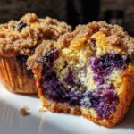A close-up of a blueberry muffin cut in half showing moist interior packed with blueberries and a crunchy streusel topping.