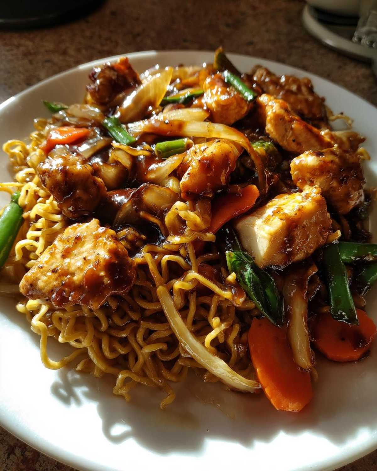 Close-up of a plate featuring the best chicken chow mein recipe with noodles, glazed chicken pieces, carrots, and onions.