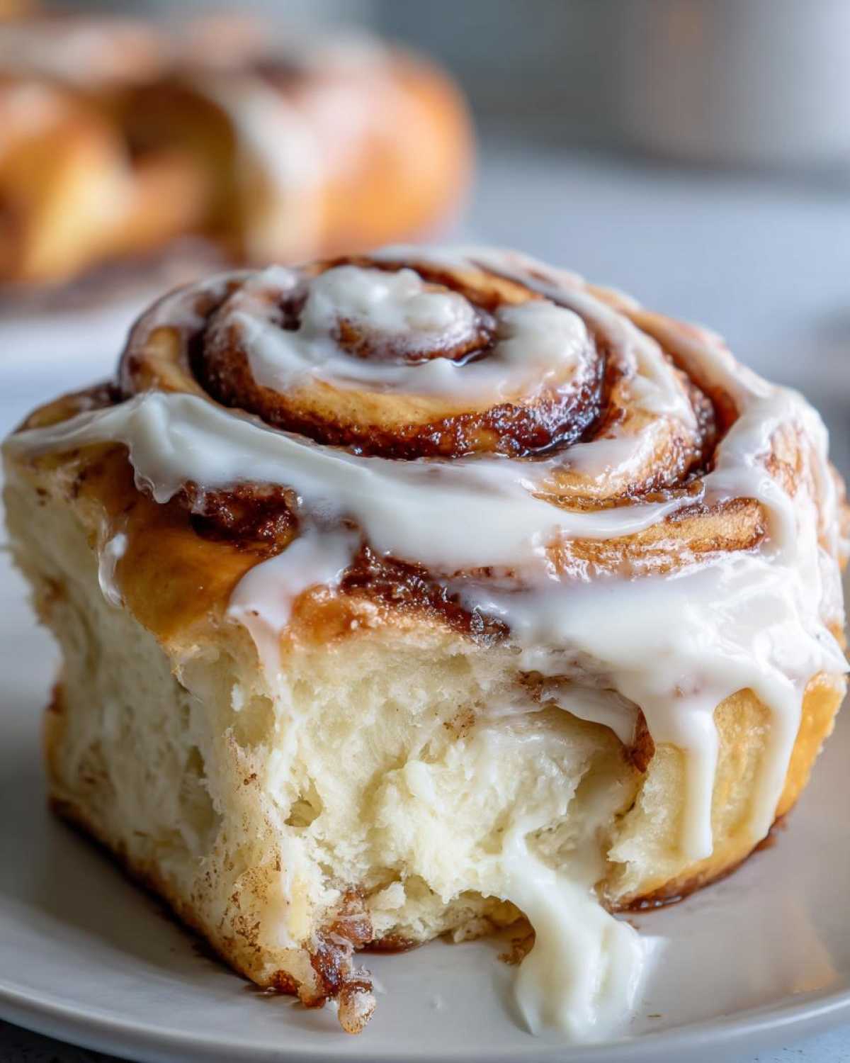 A close-up shot of a soft, fluffy cinnamon roll with rich cinnamon swirl and dripping cream cheese frosting.