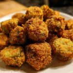 A close-up of a pile of golden brown, crispy fried okra pieces served on a white plate.