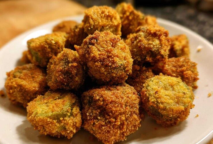 A close-up of a pile of golden brown, crispy fried okra pieces served on a white plate.