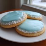 Three round sugar cookies topped with smooth, light blue sugar cookie icing and white nonpareils border.