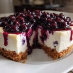 A close-up of a slice removed from a rich blueberry cheesecake, showing the creamy filling and graham cracker crust.
