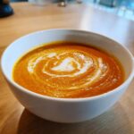 Close-up of a bowl of vibrant orange butternut squash soup topped with a white cream swirl.