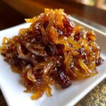 A close-up of a mound of deep amber caramelized onions served on a small white rectangular dish.