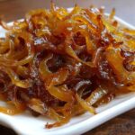 Close-up of rich, glossy, deep brown caramelized onions piled high on a small white dish.