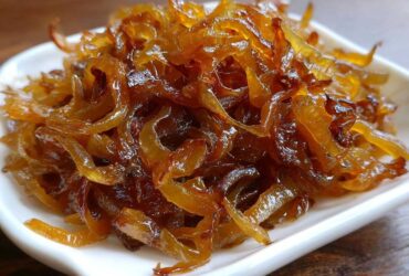 Close-up of rich, glossy, deep brown caramelized onions piled high on a small white dish.
