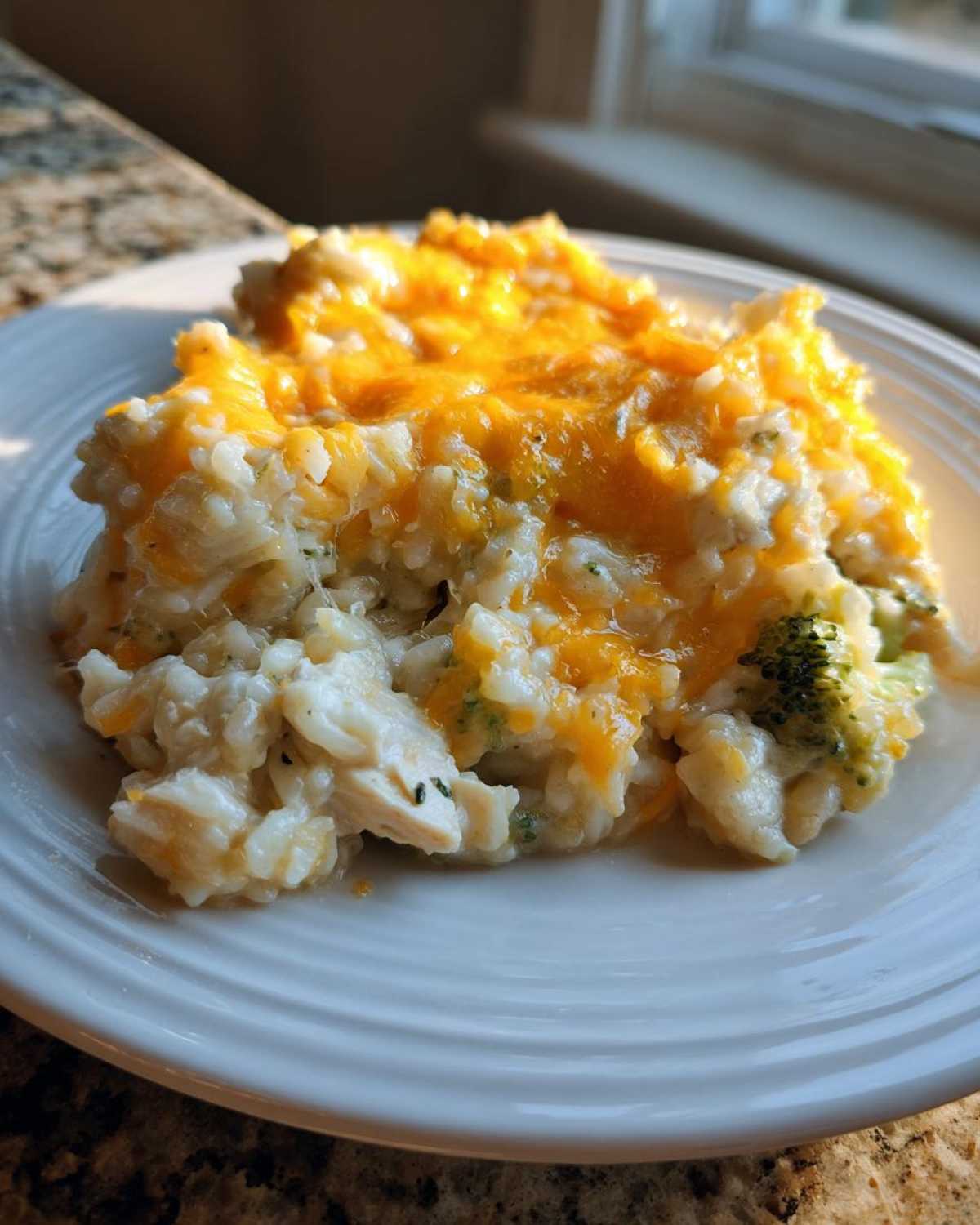 A close-up serving of cheesy chicken and rice casserole topped with melted orange cheddar cheese.