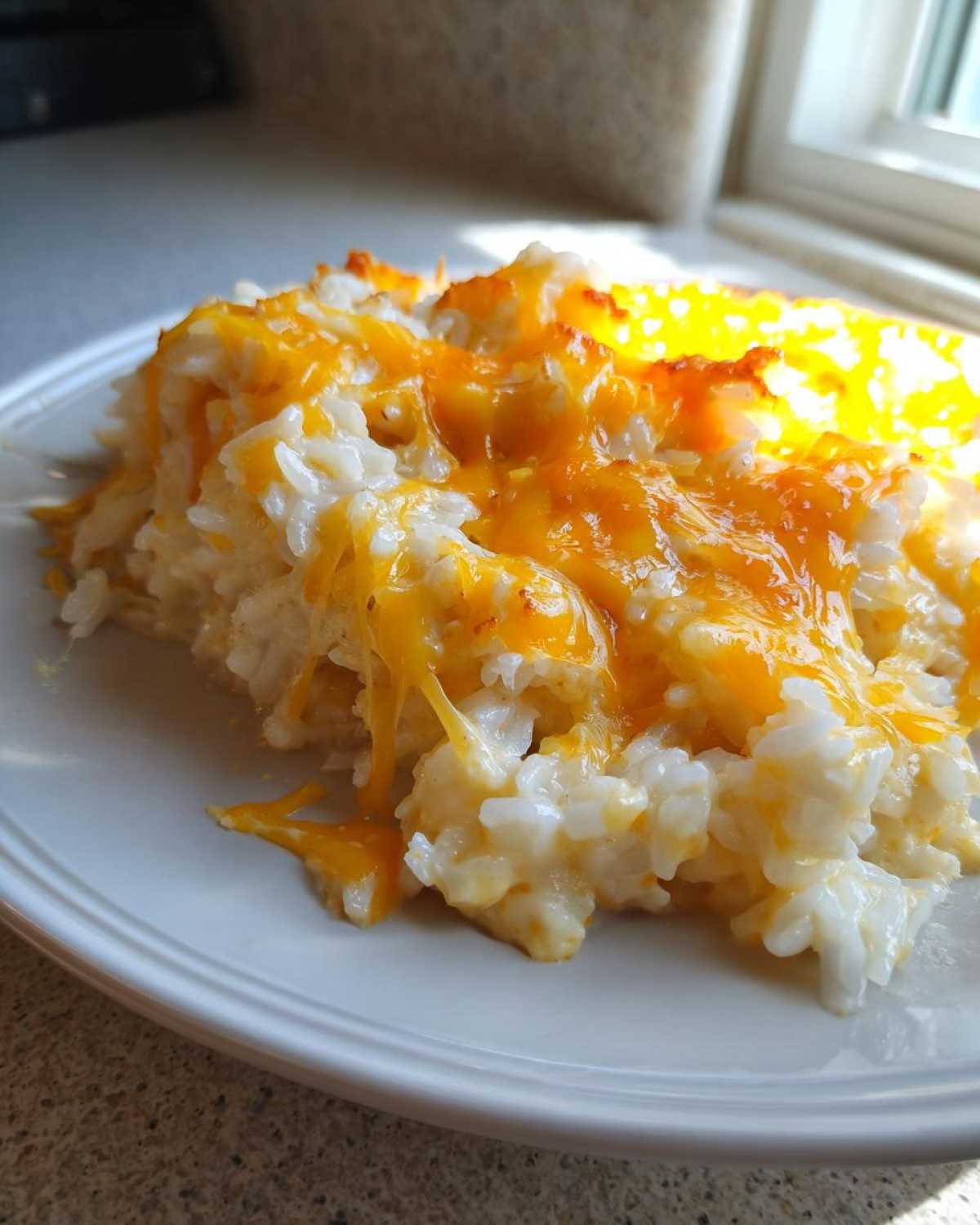 A close-up of a serving of creamy cheesy rice topped with melted, gooey orange cheddar cheese.