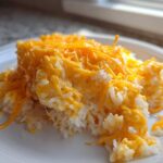 A serving of creamy, white rice topped generously with melted, bright orange cheddar cheese, making a perfect cheesy rice dish.