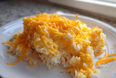 A serving of creamy, white rice topped generously with melted, bright orange cheddar cheese, making a perfect cheesy rice dish.