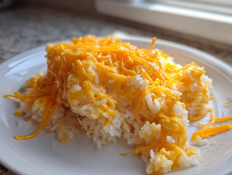 A serving of creamy, white rice topped generously with melted, bright orange cheddar cheese, making a perfect cheesy rice dish.