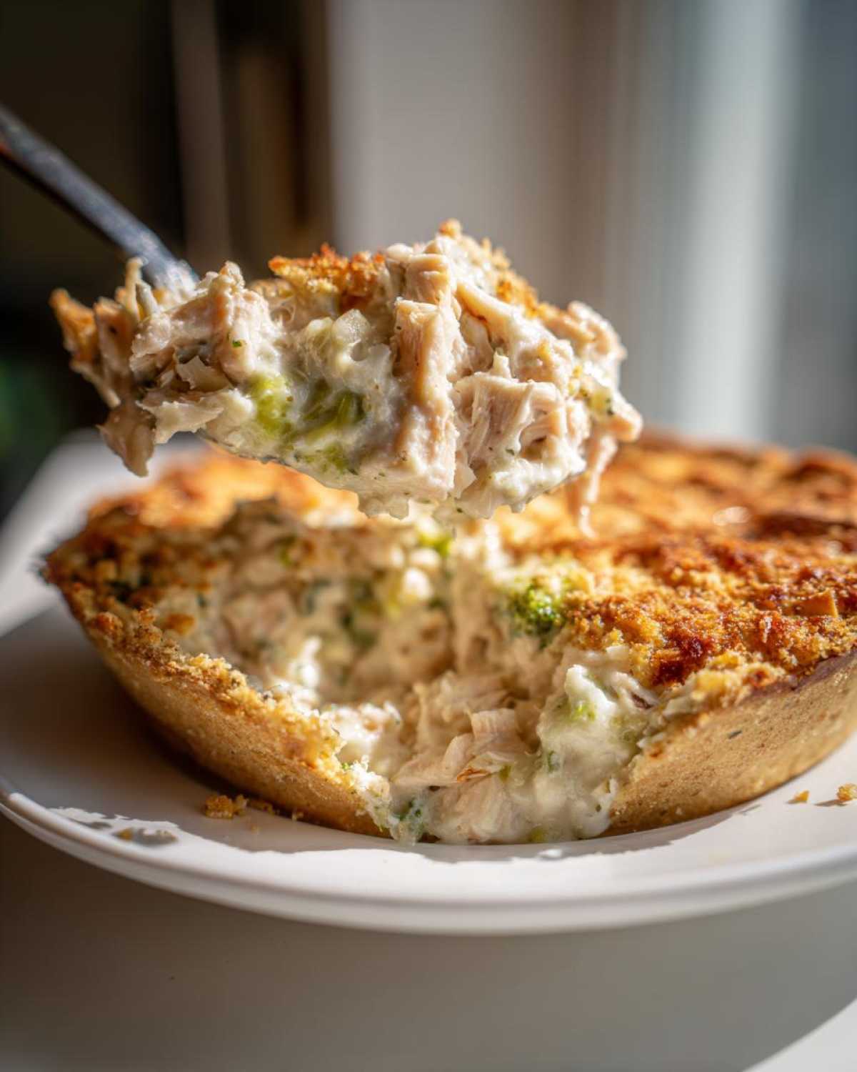 A spoonful of creamy chicken broccoli rice casserole being lifted from the main dish, showing shredded chicken and broccoli.