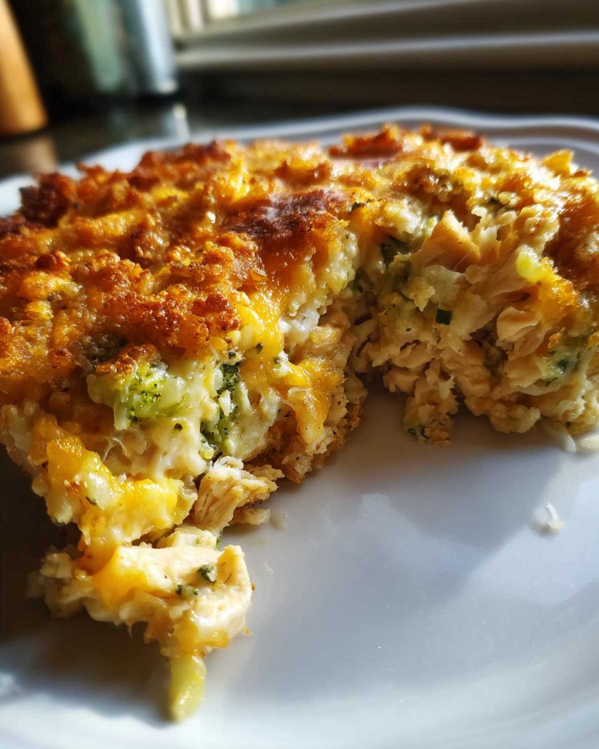 A close-up of a serving of creamy chicken broccoli rice casserole topped with melted, browned cheese.