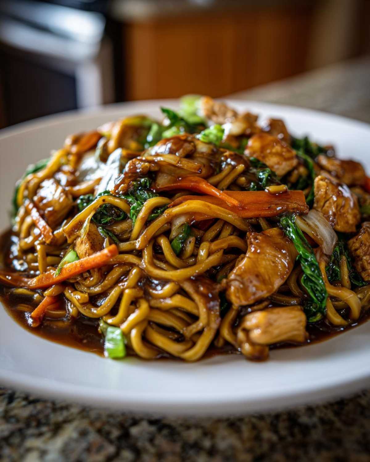 Close-up of a delicious plate of chicken chow mein recipe, featuring noodles, chicken pieces, and stir-fried vegetables in a dark sauce.