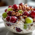 A glass bowl filled with creamy chicken salad chick grape salad, topped generously with red and green grapes and chopped pecans.
