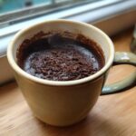 Close-up of a rich, dark chocolate mug cake topped with cocoa powder crumbs, served in a light green ceramic mug.