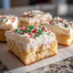 A close-up of a square portion of soft christmas sugar cookie bars topped with thick white frosting and red and green sprinkles.