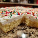 Close-up of thick christmas sugar cookie bars topped with white frosting and colorful holiday sprinkles.