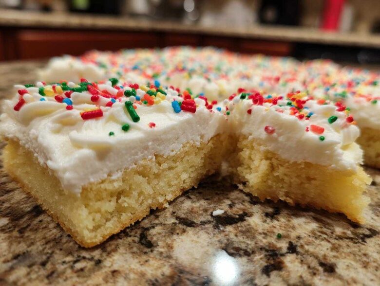 Close-up of thick christmas sugar cookie bars topped with white frosting and colorful holiday sprinkles.