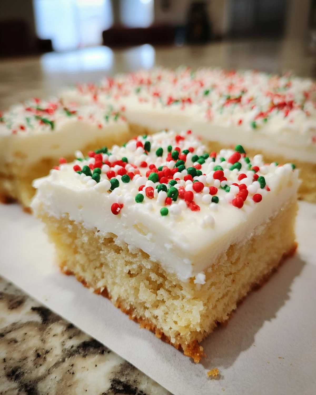 A close-up of a square slice of christmas sugar cookie bars topped with white frosting and red and green sprinkles.