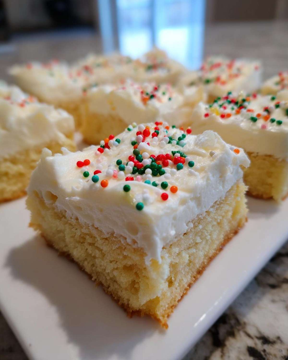 A close-up of a square slice of christmas sugar cookie bars topped with thick white frosting and festive red, green, and white sprinkles.