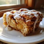 A close-up of a square slice of cinnamon roll apple pie topped with thick white icing.