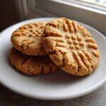 Three classic peanut butter cookies with a distinct criss-cross fork pattern stacked on a white plate.