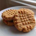 Close-up of three classic peanut butter cookies stacked on a white plate, showing the traditional crisscross fork pattern.