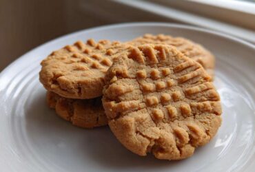 Close-up of three classic peanut butter cookies stacked on a white plate, showing the traditional crisscross fork pattern.