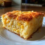 A close-up of a moist slice of corn casserole featuring visible whole corn kernels and a golden-brown top.
