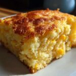 Close-up of a moist, golden slice of corn casserole featuring visible kernels of corn.