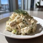 A mound of creamy cottage cheese chicken salad mixed with celery and topped with fresh dill on a white plate.