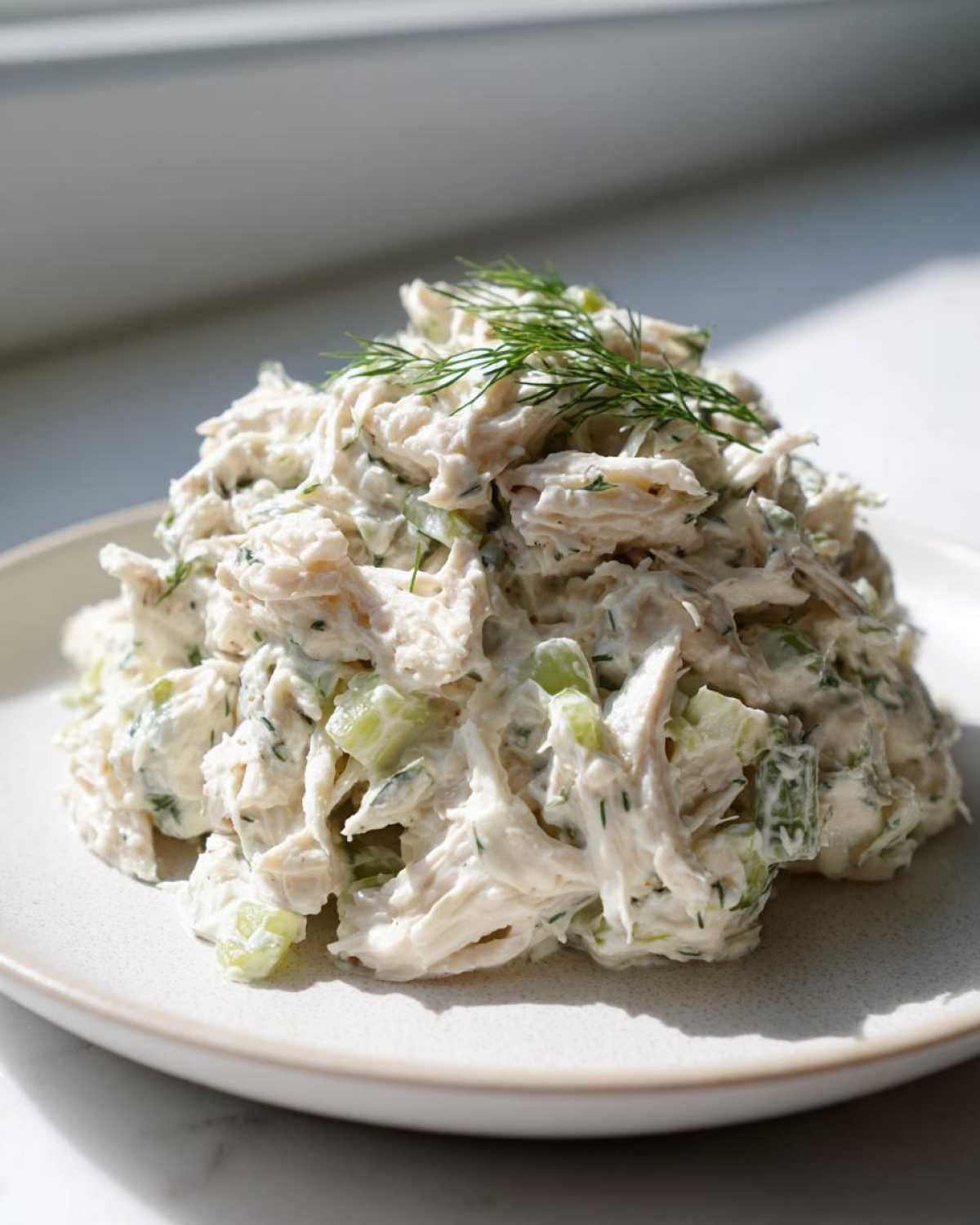 A mound of creamy cottage cheese chicken salad mixed with celery and topped with fresh dill.