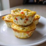 Stack of four baked cottage cheese egg cups with visible peppers and herbs on a white plate.