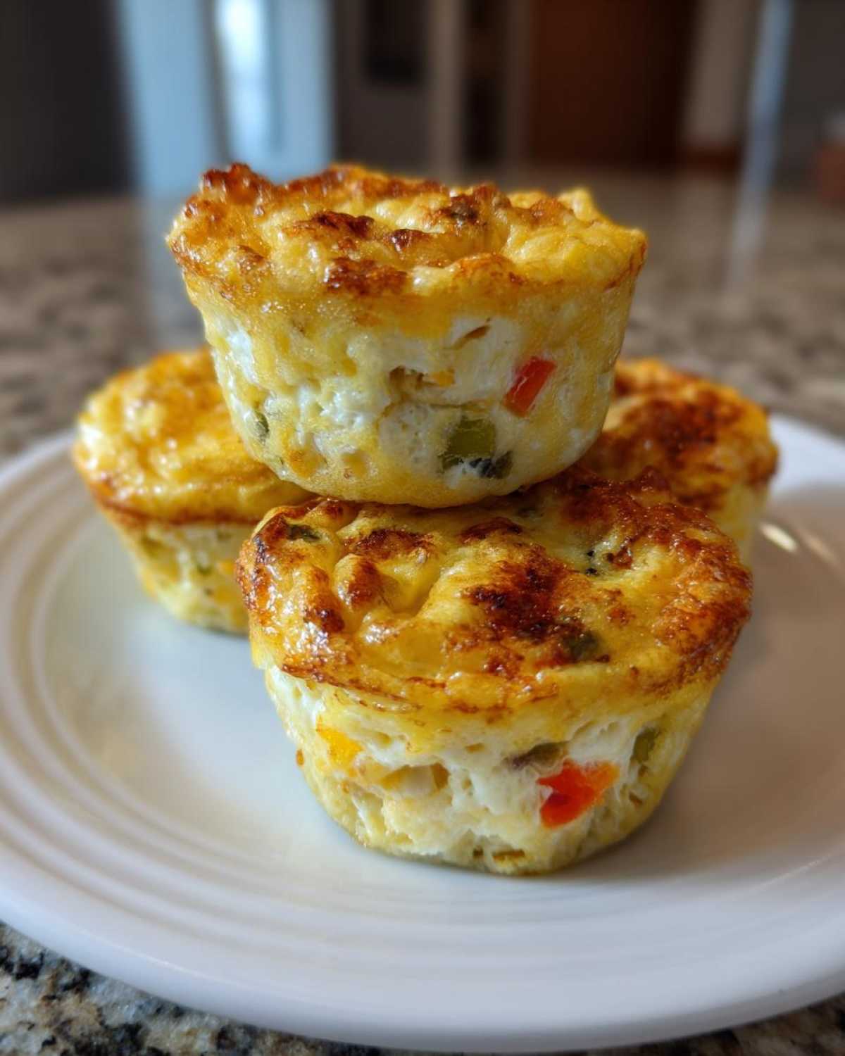 Three golden brown cottage cheese egg cups stacked on a white plate, showing visible peppers inside.