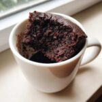 Close-up of a rich, dark chocolate Cottage Cheese Microwave Brownie sticking out of a white mug.
