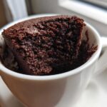 Close-up of a rich, dark chocolate Cottage Cheese Microwave Brownie sticking out of a white mug.